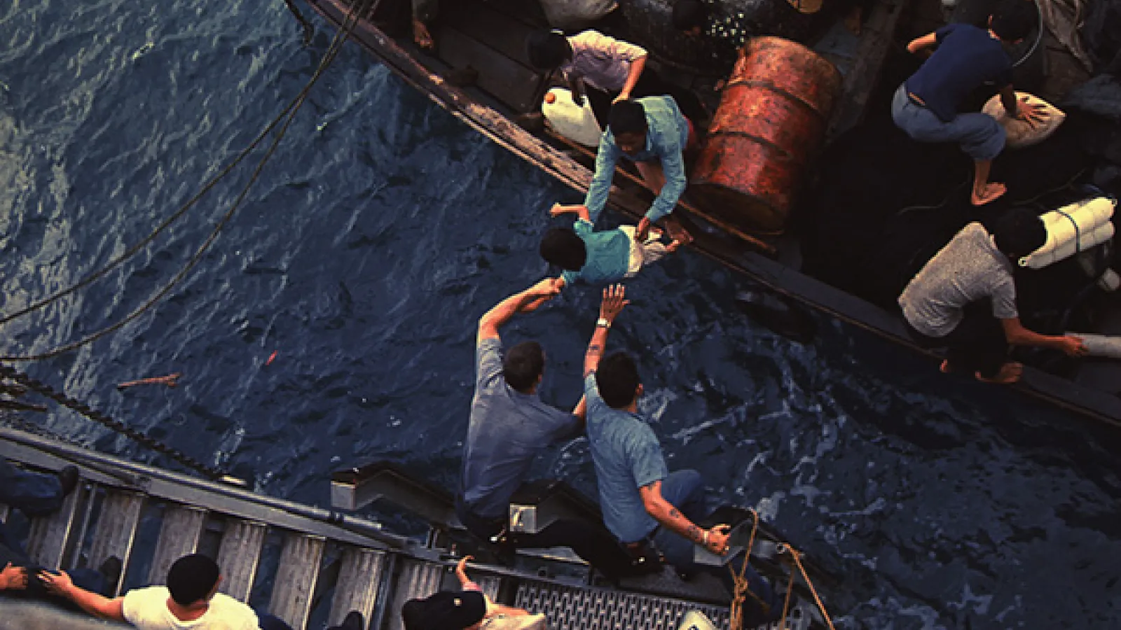 Crew on the USS Durham help Vietnamese refugees from a small craft onto their vessel in the South China Sea, 1975. Public Domain.