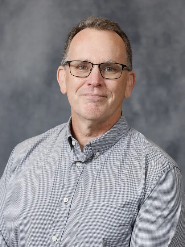 Portrait of Nick Breyfogle smiling in front of a mottled gray background